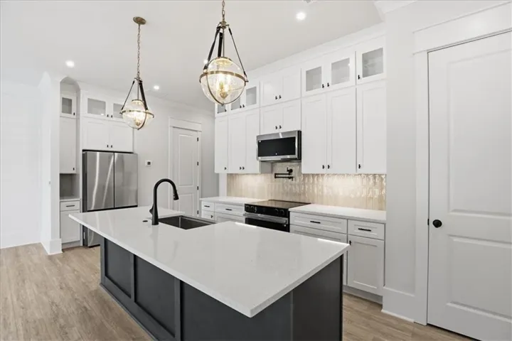 Modern kitchen featuring a large island with a substantial countertop, white cabinetry with glass-front accents, stainless steel appliances, and wood-finish flooring