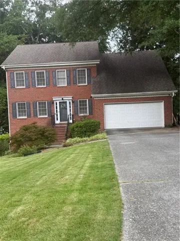 Traditional brick exterior with white trim, a two-car garage, and a manicured lawn