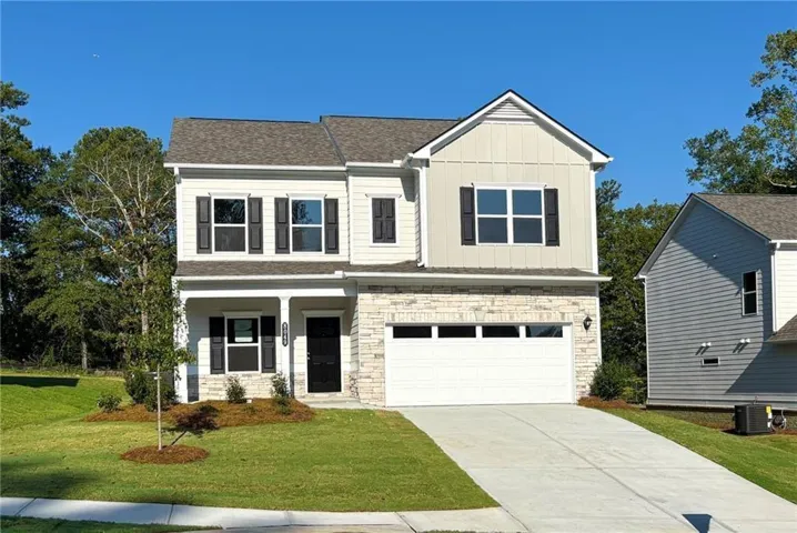 Classic two-story home featuring a clean white exterior with stone accents, two-car garage with white panel doors, and a manicured front lawn with mature landscaping