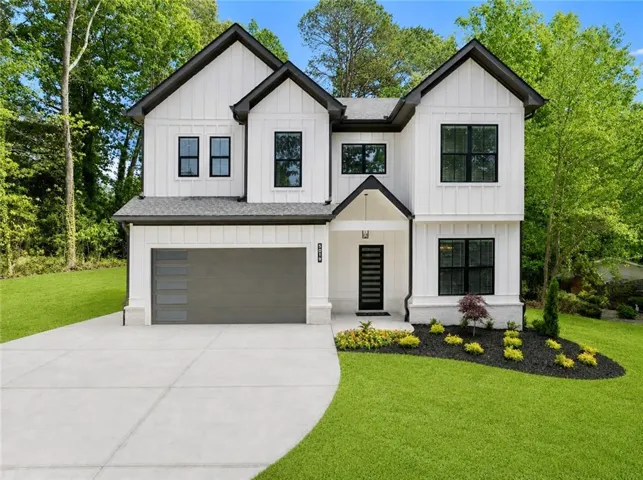 Contemporary architecture featuring a white board and batten exterior, dark trim accents, a modern garage door, a prominent front entry with a dark door, and a landscaped front yard with a concrete driveway