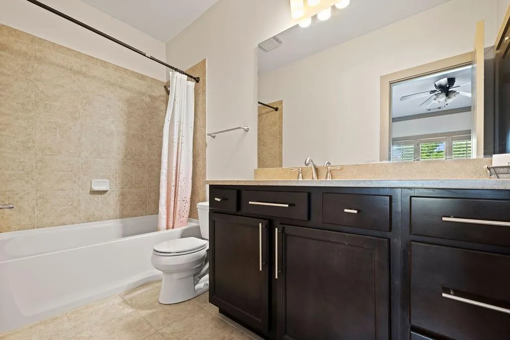 Full bathroom with toilet, shower / tub combo with curtain, ceiling fan, tile patterned flooring, and vanity