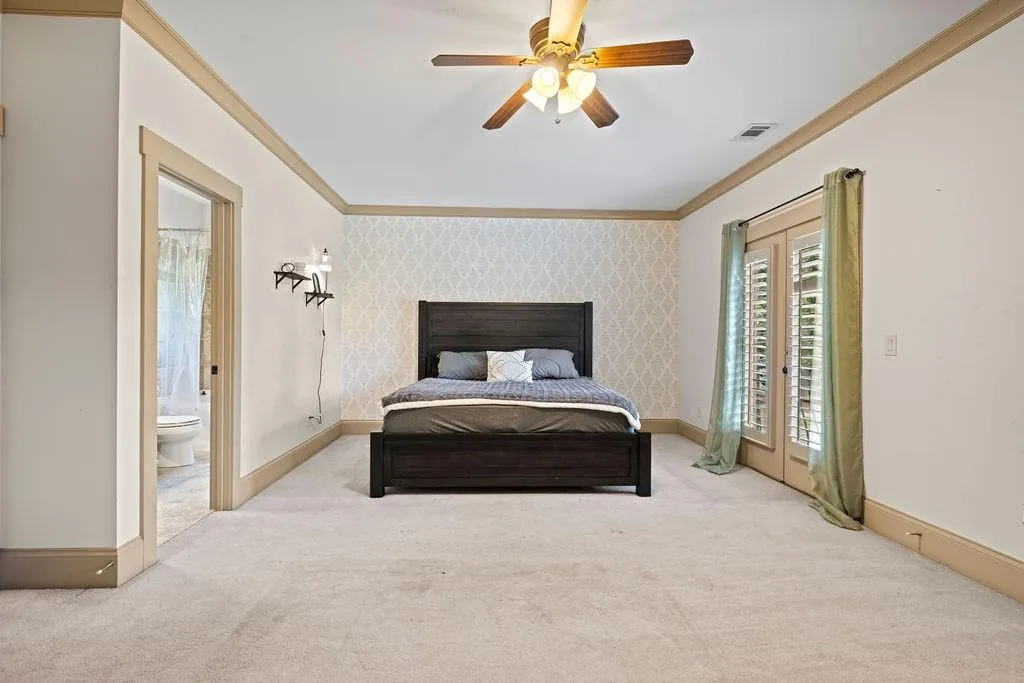 Bedroom featuring ceiling fan, french doors, ensuite bath, ornamental molding, and light colored carpet