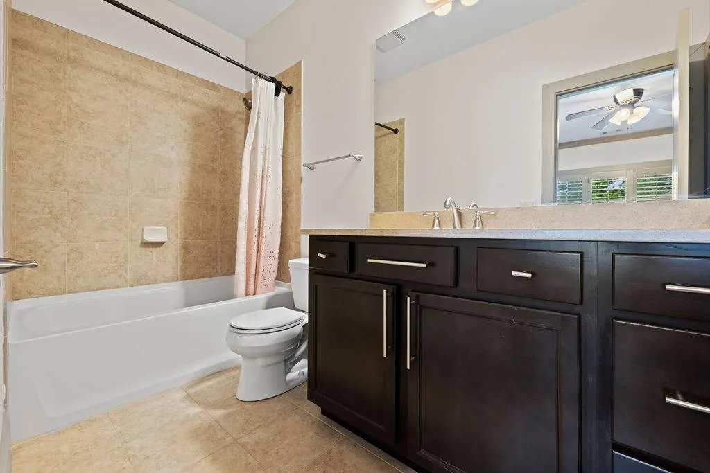 Full bathroom with ceiling fan, toilet, vanity, tile patterned flooring, and shower / bathtub combination with curtain