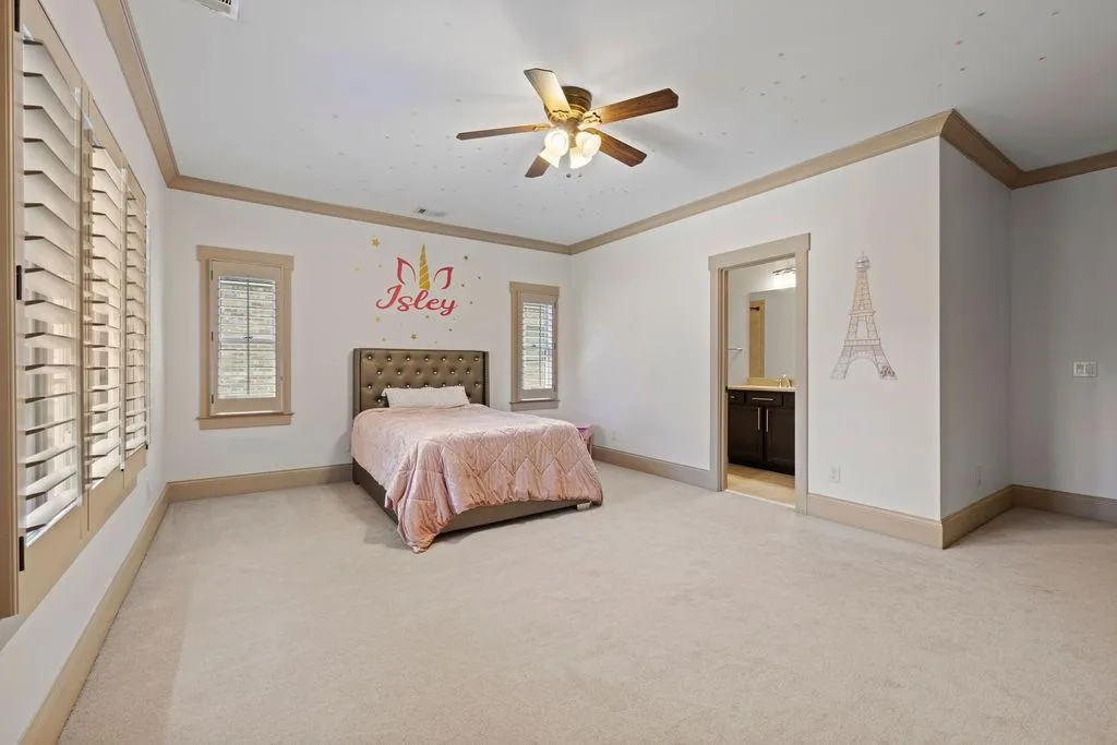 Carpeted bedroom featuring ceiling fan, ensuite bath, and ornamental molding