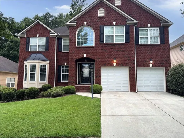 Brick exterior residence featuring a prominent arched window, a bay window with a dark metal roof, and a two-car garage