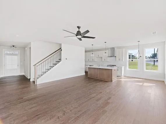 Expansive open-concept living area featuring wood-finish flooring, a contemporary kitchen with white cabinetry and a central island, a modern ceiling fan, and large windows