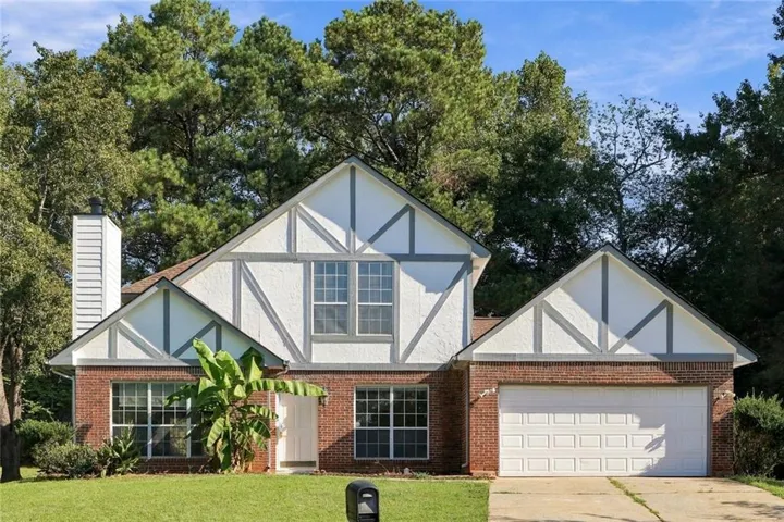 Brick and stucco exterior with decorative timber framing, a two-car garage, multiple gables, and a prominent chimney