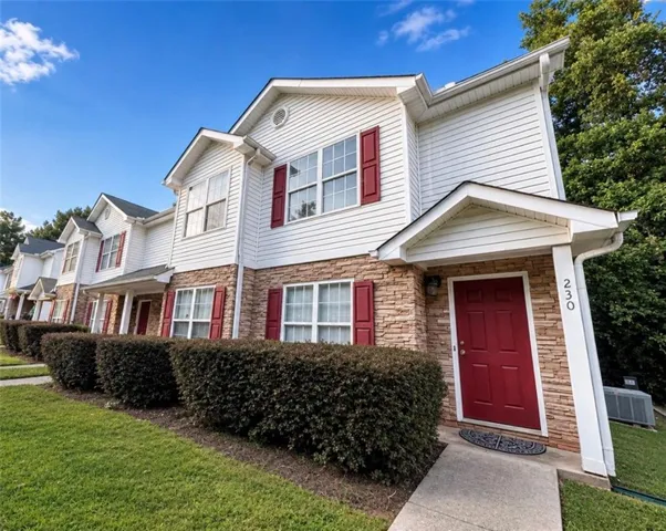 Exterior featuring white siding, stone veneer accents, a red entry door, and red window shutters