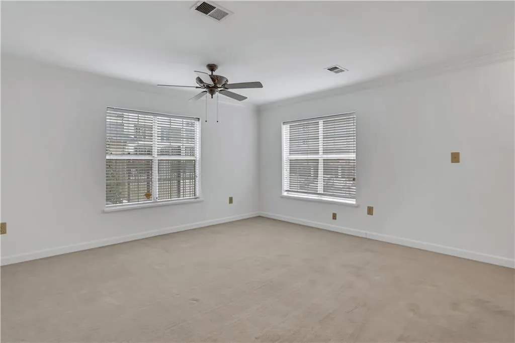 Spare room with light colored carpet, healthy amount of natural light, ornamental molding, and ceiling fan