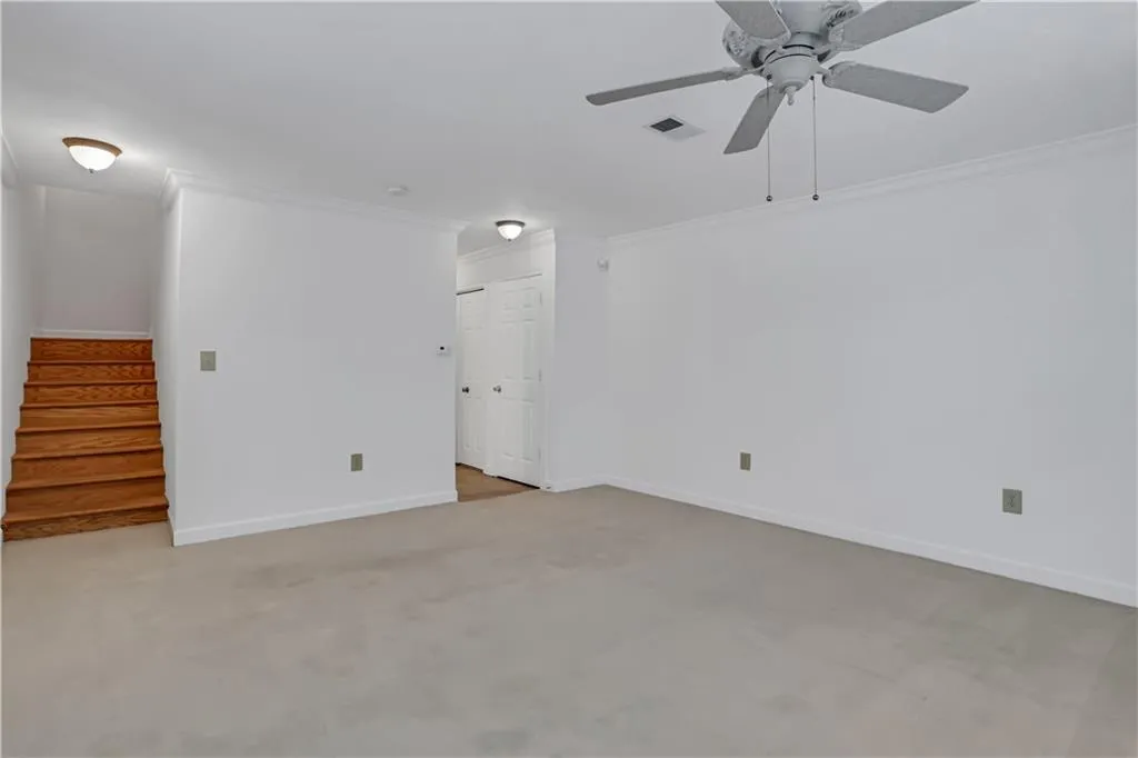 Empty room featuring crown molding, light colored carpet, stairs, and ceiling fan