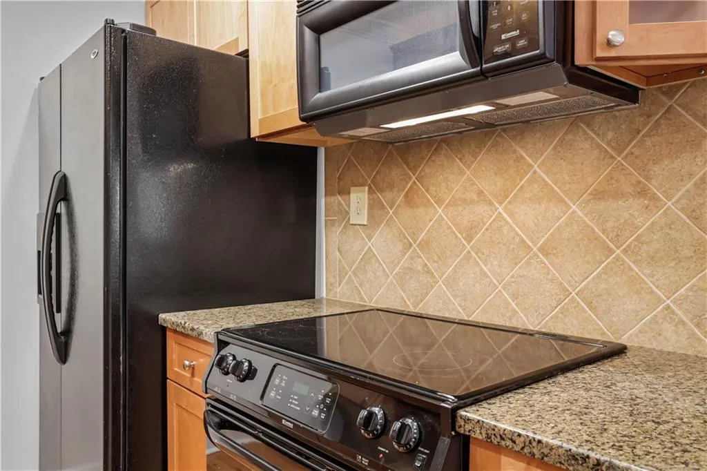 Kitchen featuring black appliances, decorative backsplash, light stone counters, and light brown cabinets