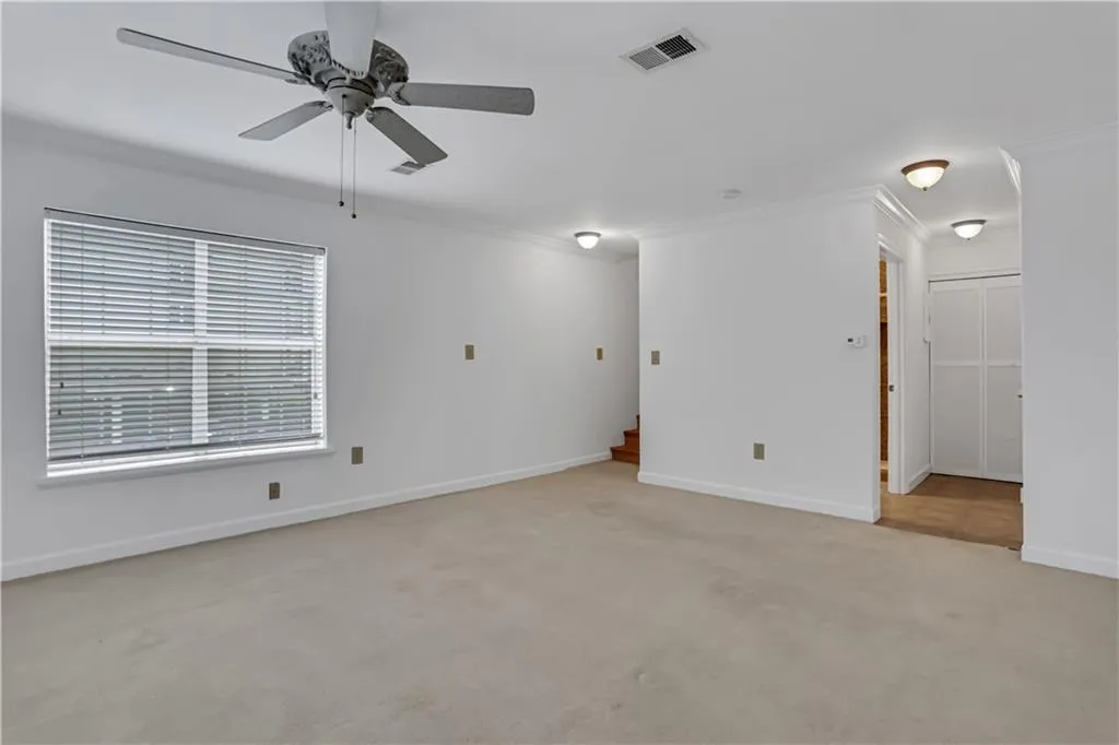 Empty room featuring light colored carpet, ornamental molding, and a ceiling fan