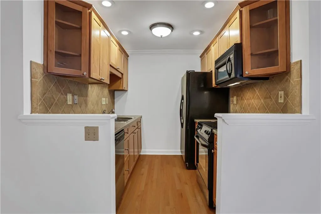 Kitchen with range with electric stovetop, light wood finished floors, open shelves, black microwave, and decorative backsplash