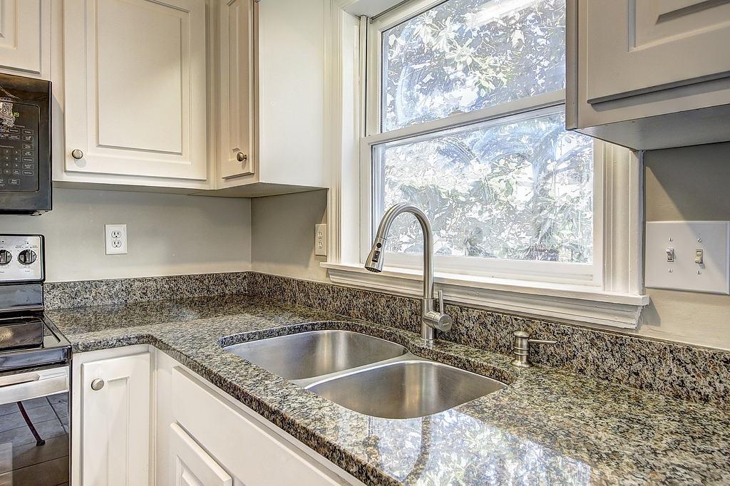 Kitchen with black microwave, white cabinets, sink, dark stone countertops, and stainless steel range with electric stovetop