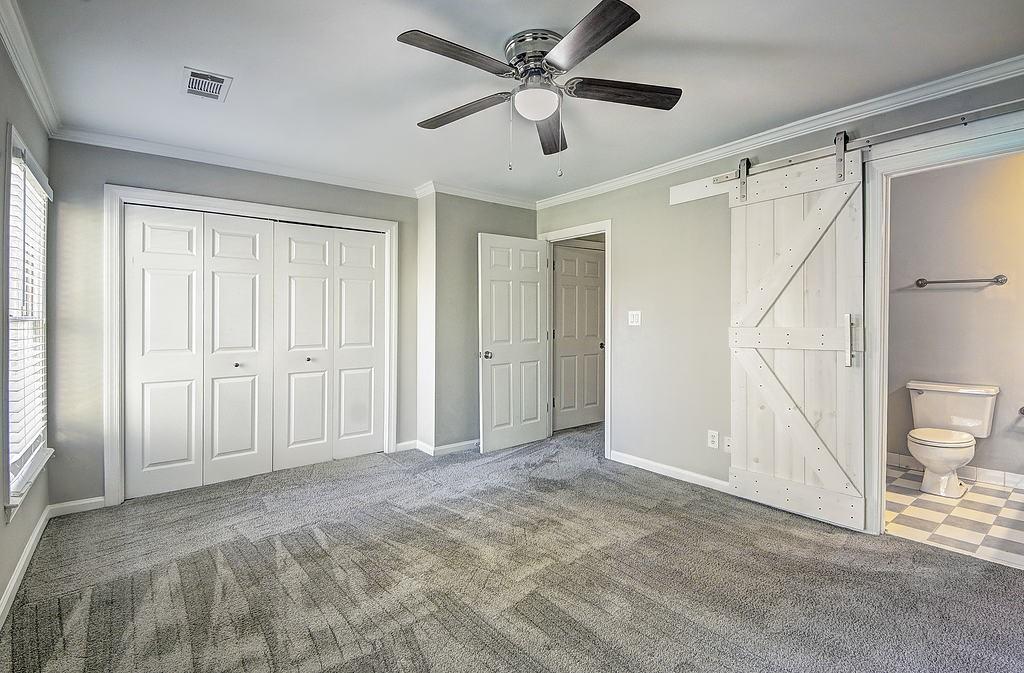 Unfurnished bedroom with ensuite bath, a barn door, dark carpet, and ceiling fan
