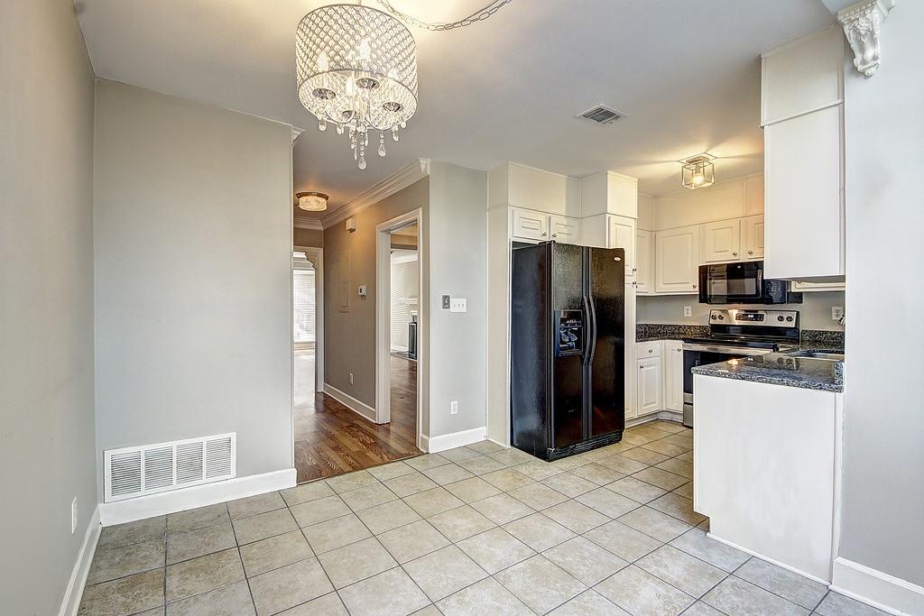 Kitchen featuring white cabinets, light tile flooring, an inviting chandelier, and black appliances