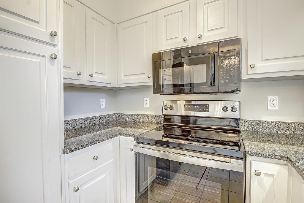 Kitchen with tile floors, stainless steel electric stove, white cabinetry, and stone countertops