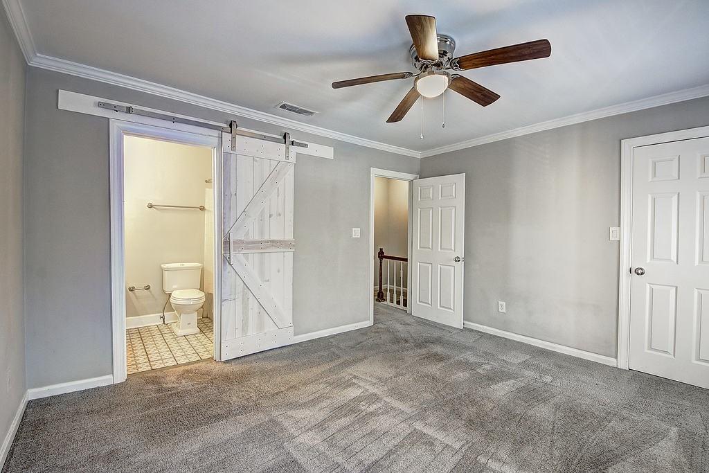 Unfurnished bedroom featuring crown molding, dark tile flooring, ceiling fan, connected bathroom, and a barn door