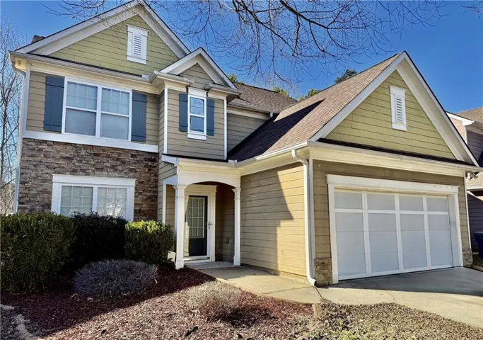 View of front of home featuring a garage, a shingled roof, concrete driveway, and stone siding