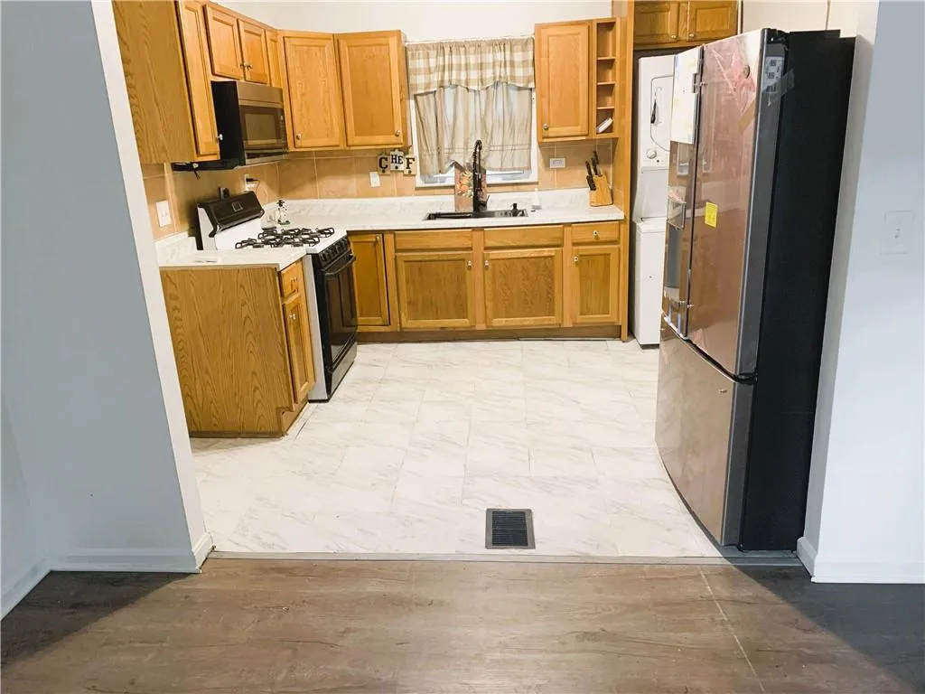 Kitchen with light countertops, appliances with stainless steel finishes, brown cabinetry, stacked washing machine and dryer, and light wood finished floors