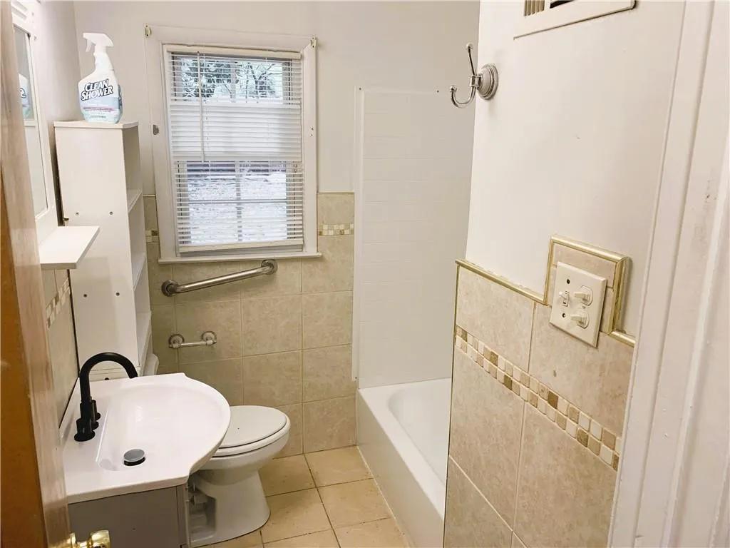 Full bathroom with tile walls, tile patterned flooring, vanity, shower / tub combination, and a wainscoted wall