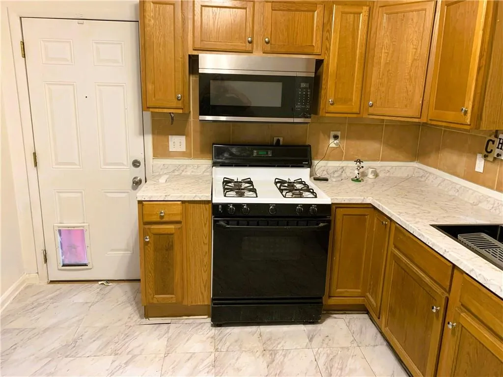 Kitchen featuring brown cabinets, black gas range, stainless steel microwave, tasteful backsplash, and light marble finish floors