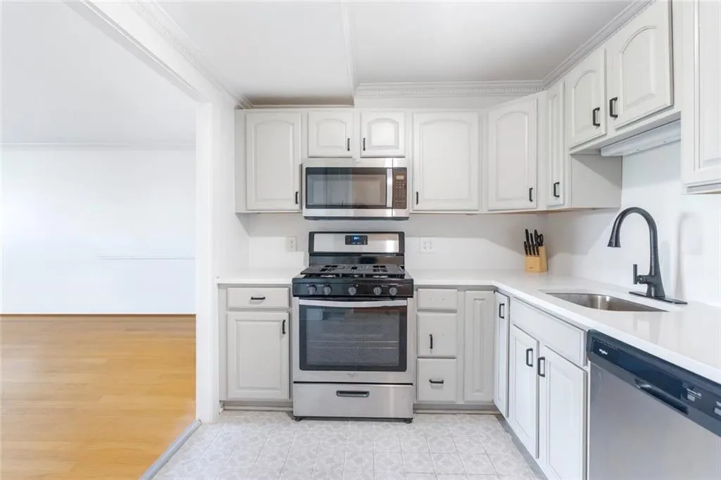 Kitchen featuring stainless steel appliances, crown molding, white cabinets, and light stone countertops