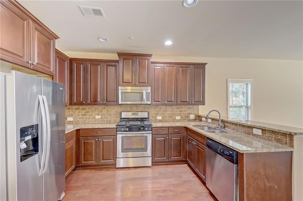 Kitchen with kitchen peninsula, light hardwood / wood-style flooring, stainless steel appliances, backsplash, and sink