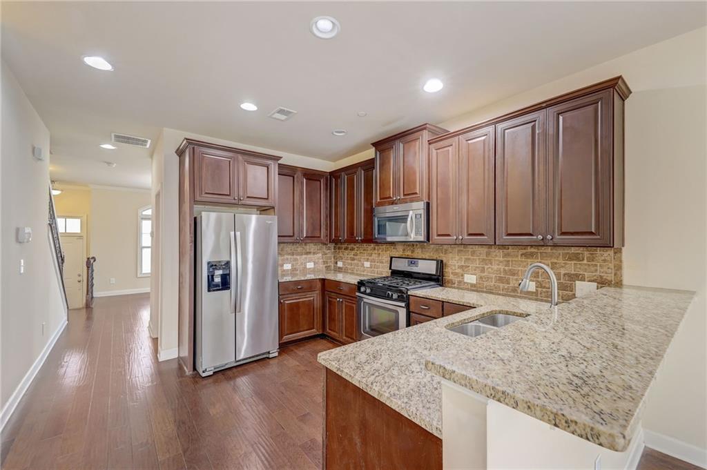 Kitchen with tasteful backsplash, dark wood-type flooring, appliances with stainless steel finishes, kitchen peninsula, and sink