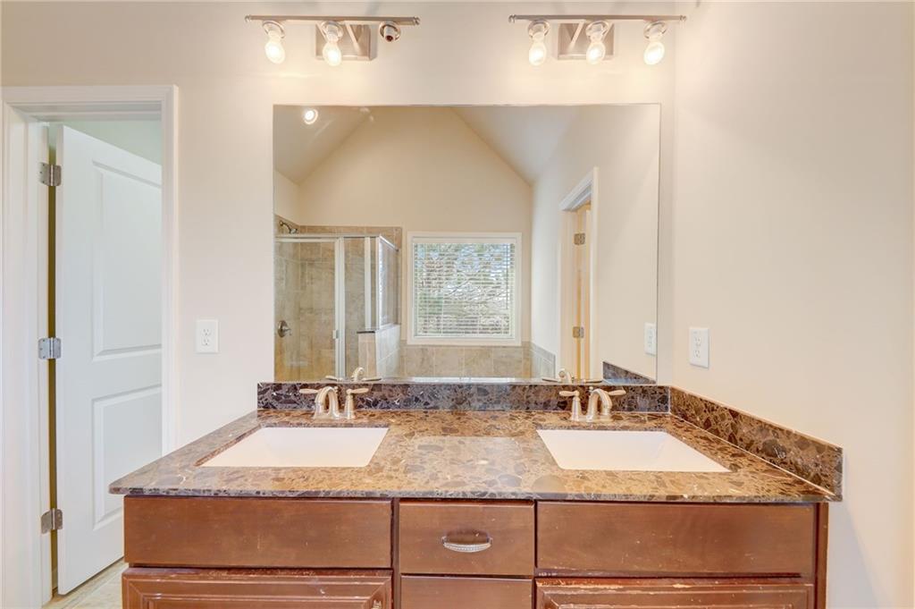 Bathroom with a shower with shower door, lofted ceiling, large vanity, and double sink