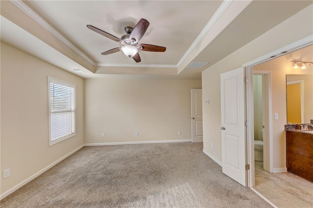 Carpeted empty room featuring a tray ceiling and ceiling fan