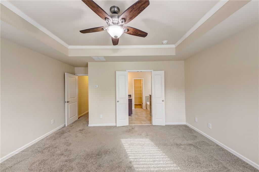 Unfurnished bedroom featuring ornamental molding, light carpet, ceiling fan, and a raised ceiling