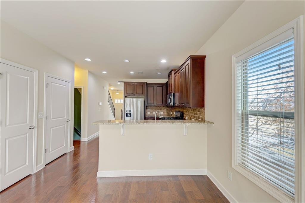 Kitchen with kitchen peninsula, light stone countertops, light hardwood / wood-style floors, appliances with stainless steel finishes, and backsplash