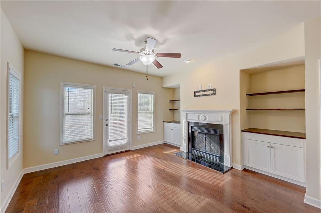 Unfurnished living room featuring a tile fireplace, built in features, dark hardwood / wood-style floors, and ceiling fan