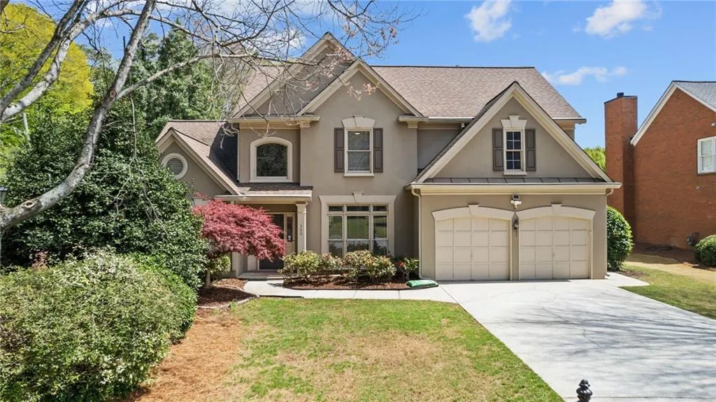 Traditional-style house featuring stucco siding, an attached garage, driveway, a front yard, and a shingled roof