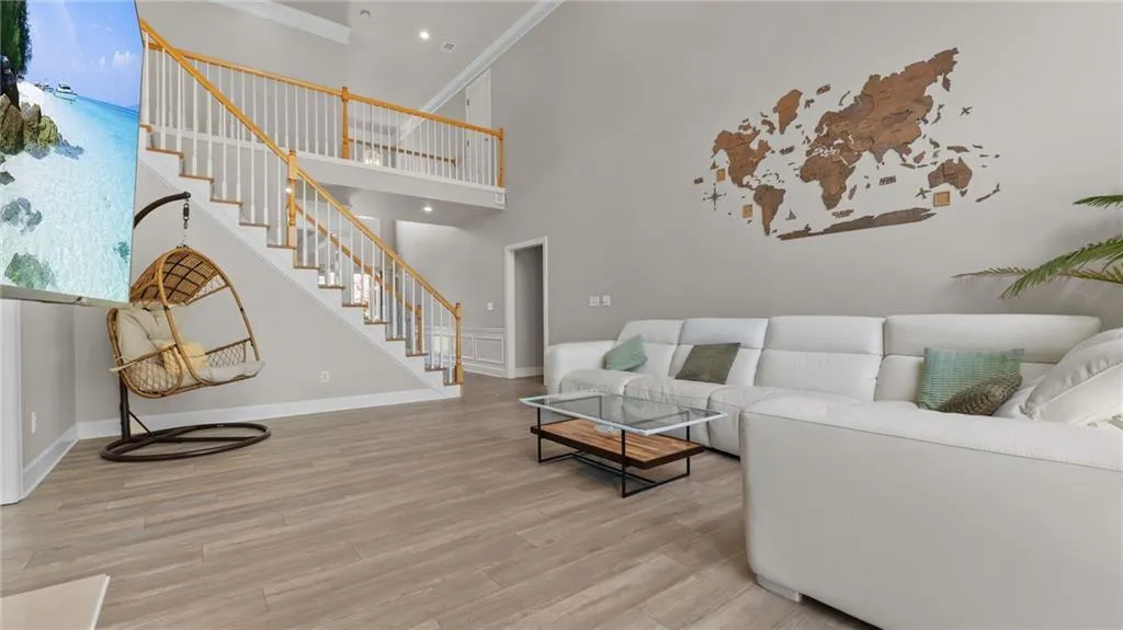 Living room with stairs, crown molding, wood finished floors, baseboards, and a towering ceiling