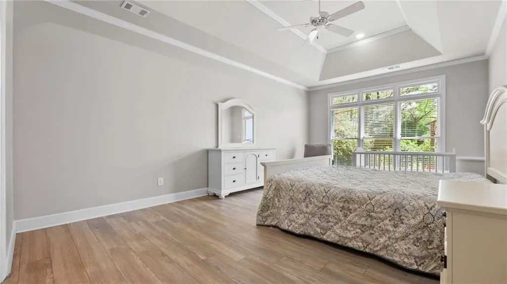 Bedroom featuring visible vents, baseboards, ornamental molding, a raised ceiling, and light wood-type flooring