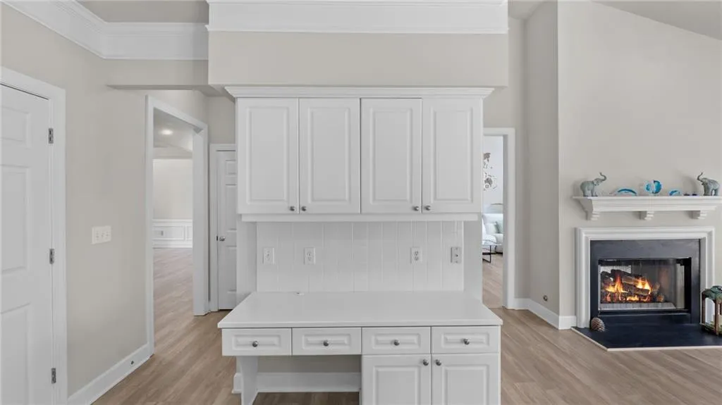 Kitchen with light countertops, crown molding, light wood finished floors, a lit fireplace, and white cabinetry