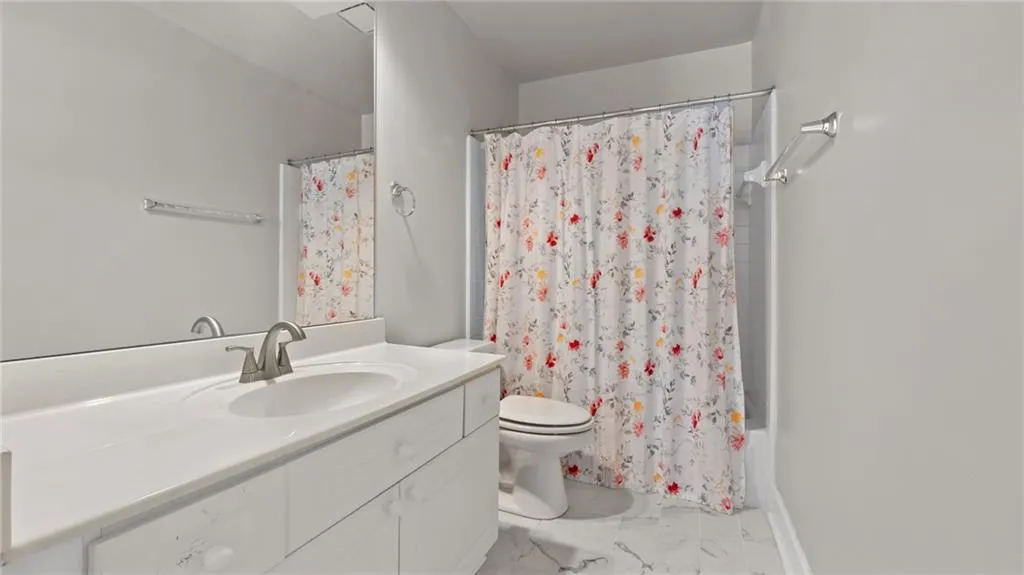 Bathroom with marble finish floor, shower / tub combo, toilet, and vanity