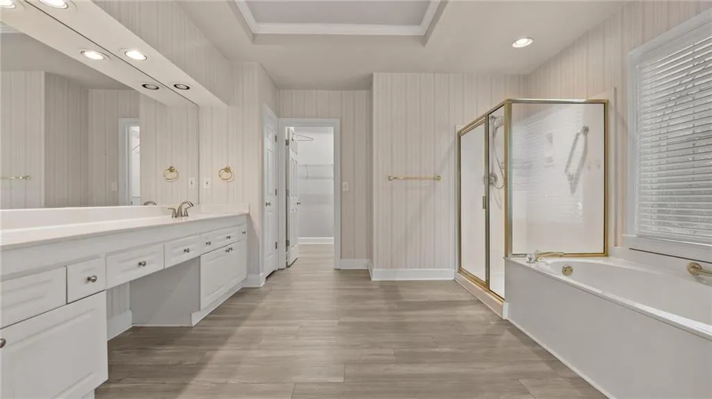 Bathroom featuring vanity, a raised ceiling, a shower stall, a garden tub, and wood finished floors
