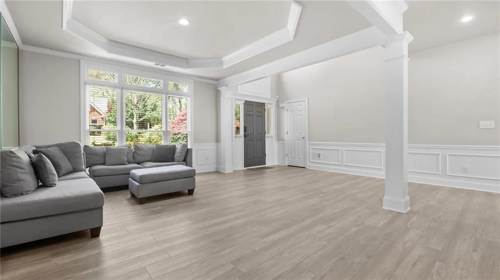 Living area with a tray ceiling, light wood-style flooring, a decorative wall, and decorative columns
