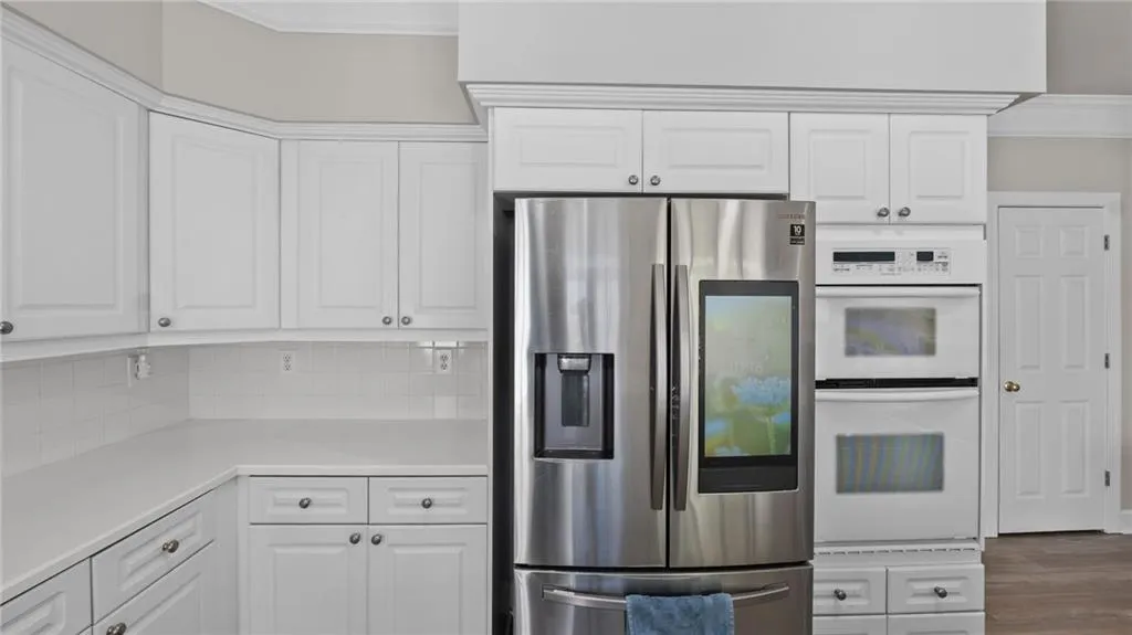 Kitchen featuring double oven, stainless steel fridge, light countertops, and white cabinets