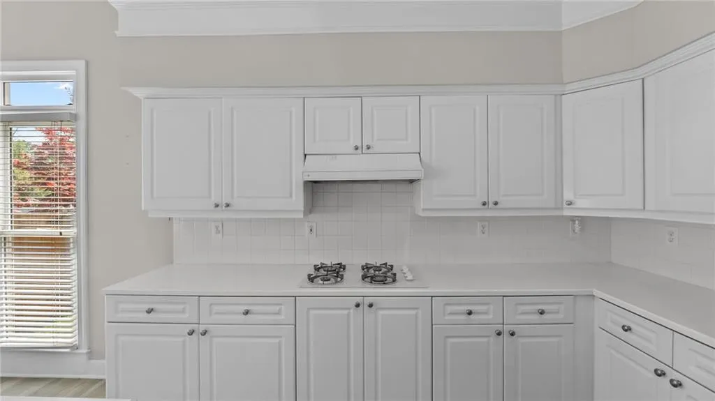 Kitchen with white cabinetry, light countertops, under cabinet range hood, and decorative backsplash