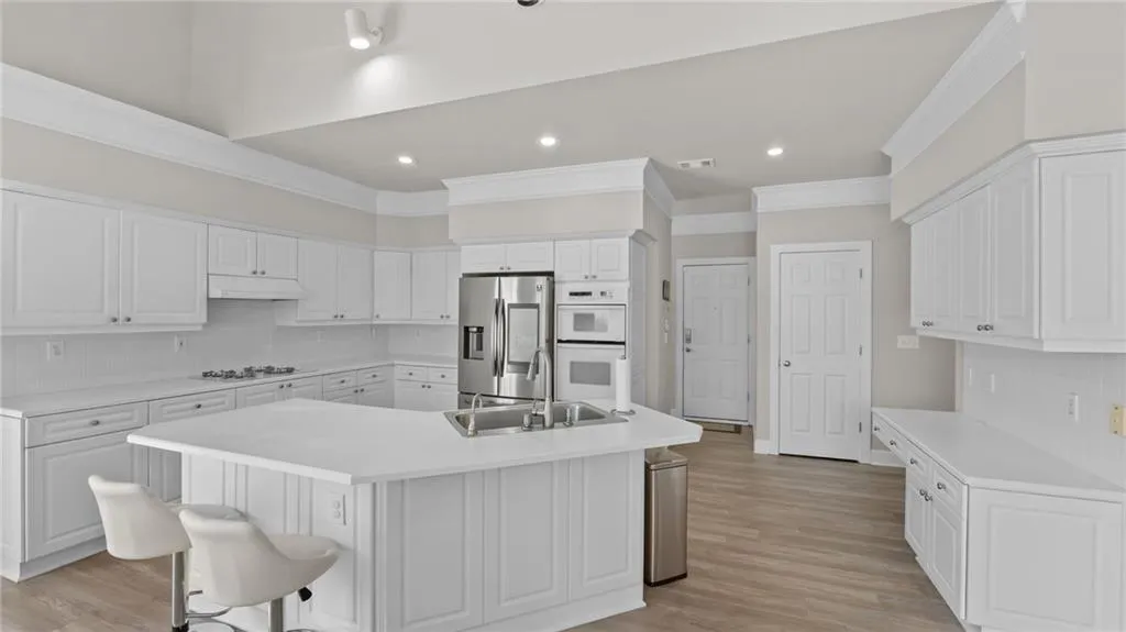Kitchen featuring white cabinets, a sink, under cabinet range hood, and white appliances