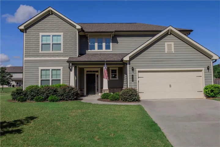 Two-story exterior with horizontal siding and shingle accents, concrete driveway, attached garage with carriage-style door, covered front entry, and established landscaping