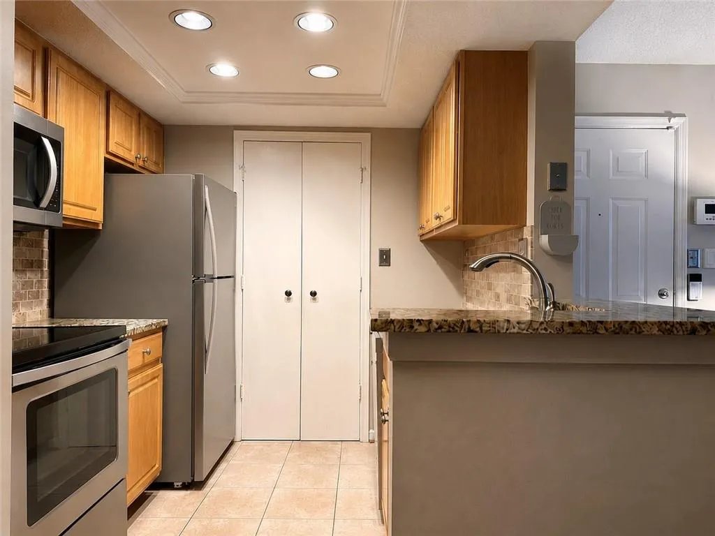 Kitchen featuring stainless steel appliances, wood cabinetry, stone countertops, and a tiled backsplash
