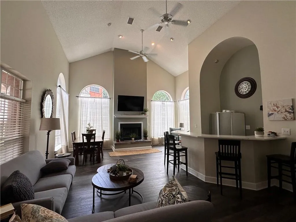 Open-concept living area featuring vaulted ceilings, wood-finish flooring, and multiple arched windows