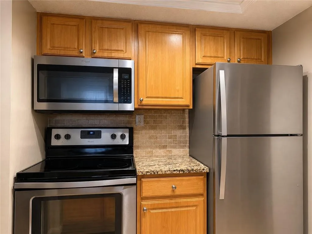 Kitchen featuring stainless steel appliances, wood cabinetry, granite-style countertops, and a tile backsplash