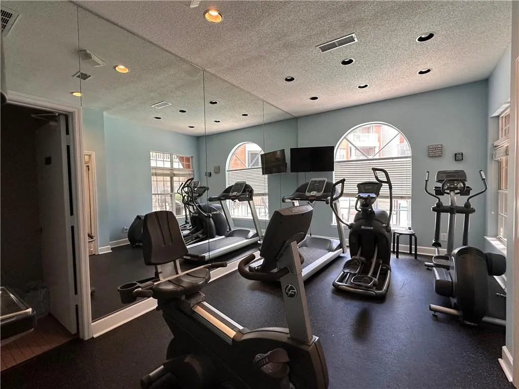 Dedicated fitness center featuring full-height mirrors, rubber flooring, and recessed lighting