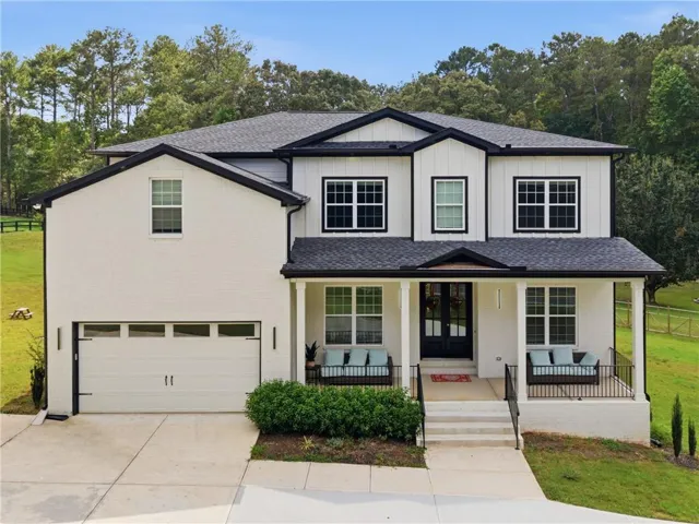 Contemporary two-story residence featuring a covered front porch, a two-car garage, white brick and board-and-batten siding, and dark-framed windows